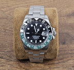 Silver watch with black dial on a brown cushion against a wooden background