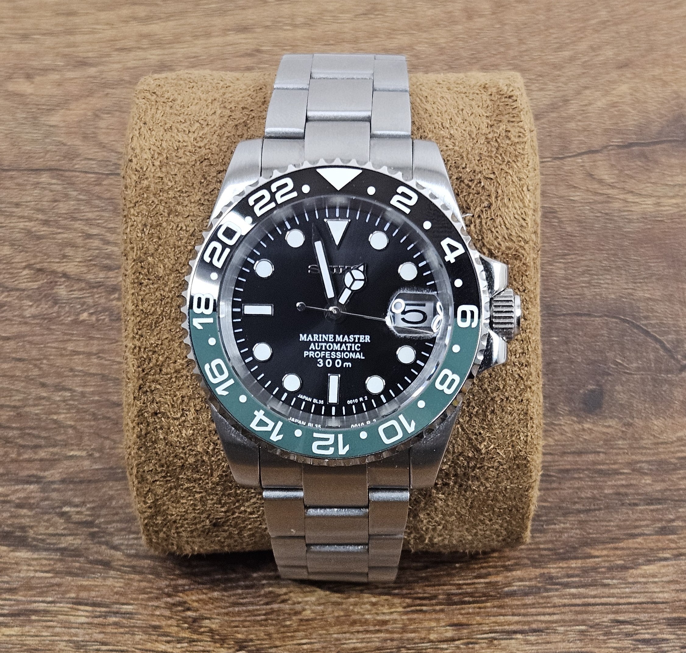 Silver watch with black dial on a brown cushion against a wooden background