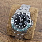 Watch with a black face and silver metal strap on a brown cushion against a wooden background