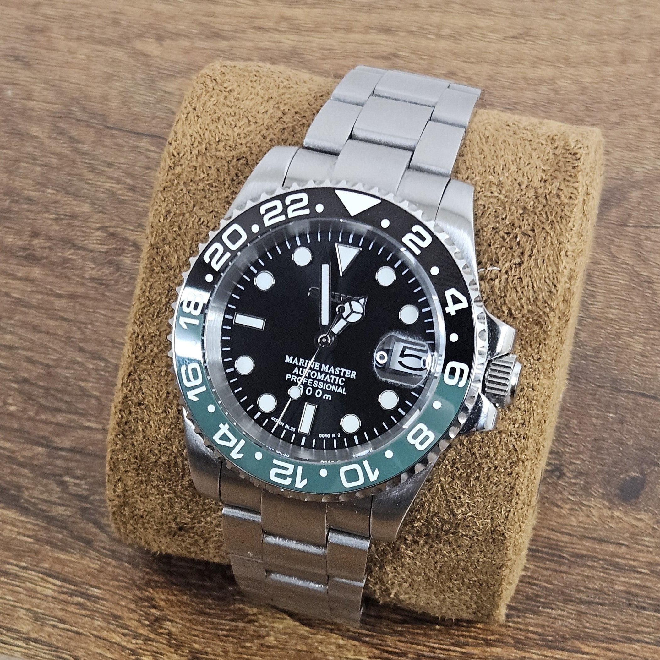 Watch with a black face and silver metal strap on a brown cushion against a wooden background