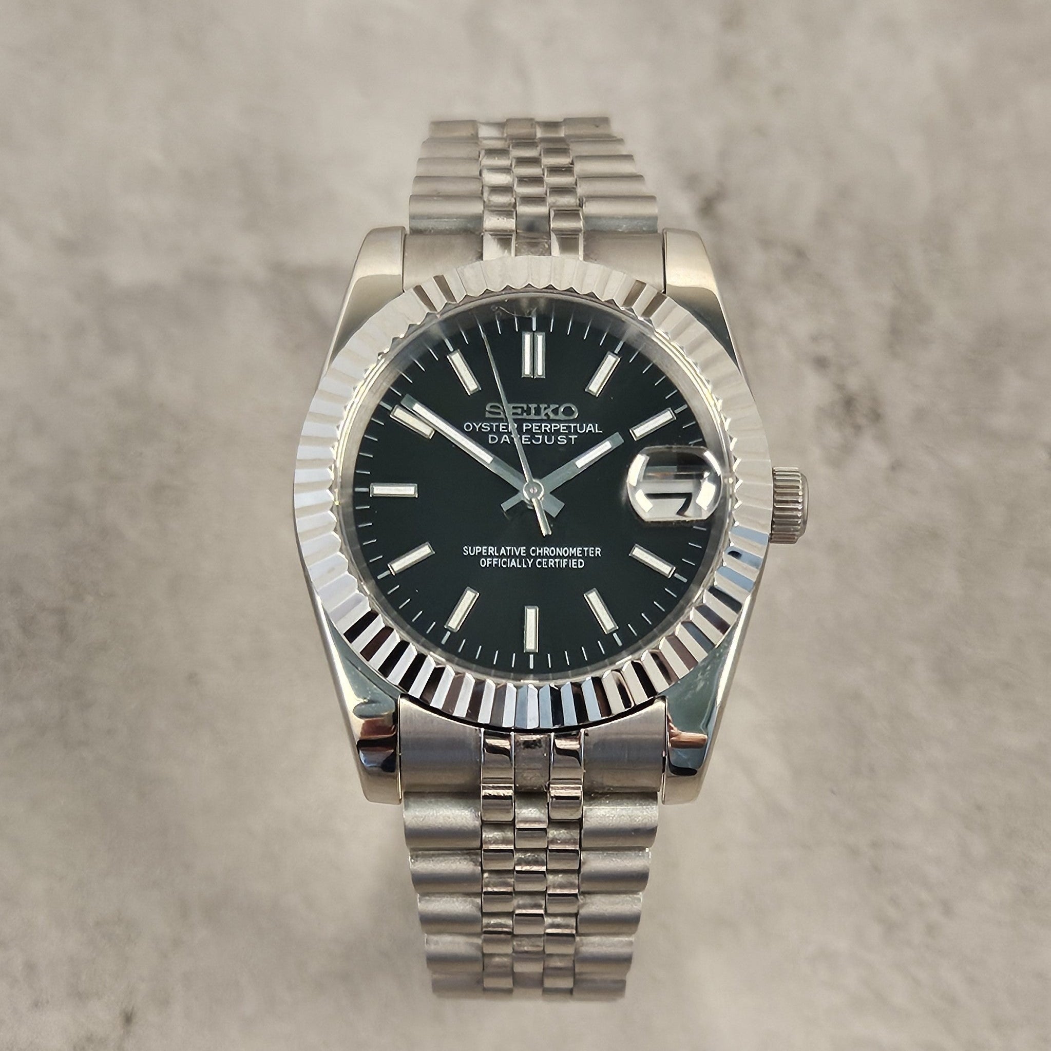 Silver Seiko watch with black dial on a gray textured background