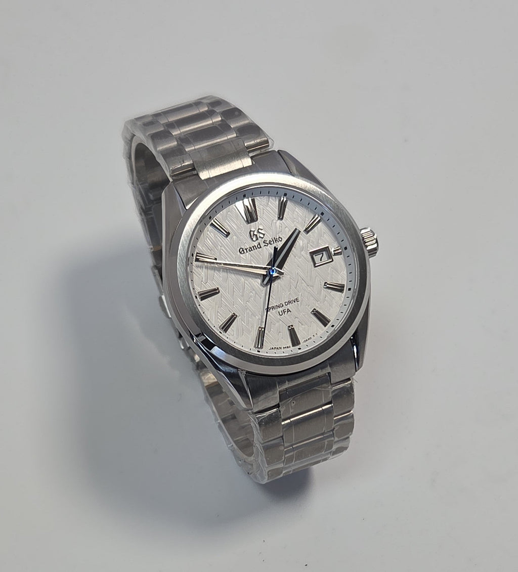 A silver stainless steel wrist watch with a textured white dial, featuring a date window, silver-tone hour markers, and a matching metal link bracelet, photographed on a light gray background.
