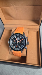 Wristwatch with orange strap and black dial in a brown box