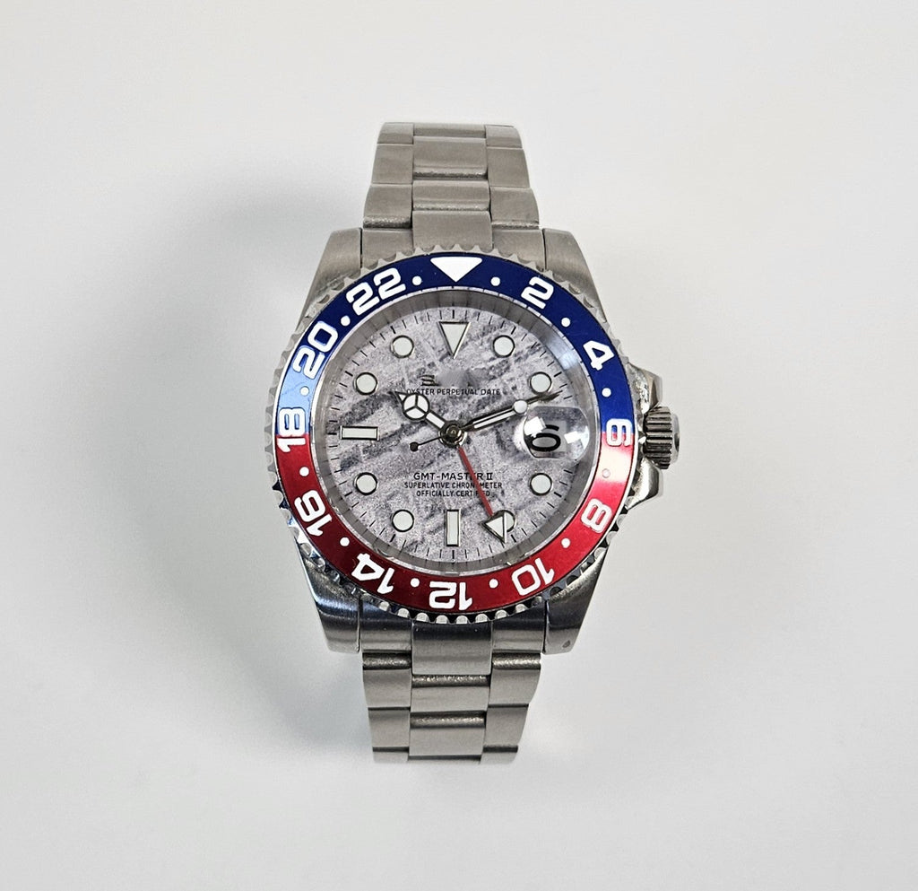 Luxury watch with a silver, blue, and red bezel on a light gray background