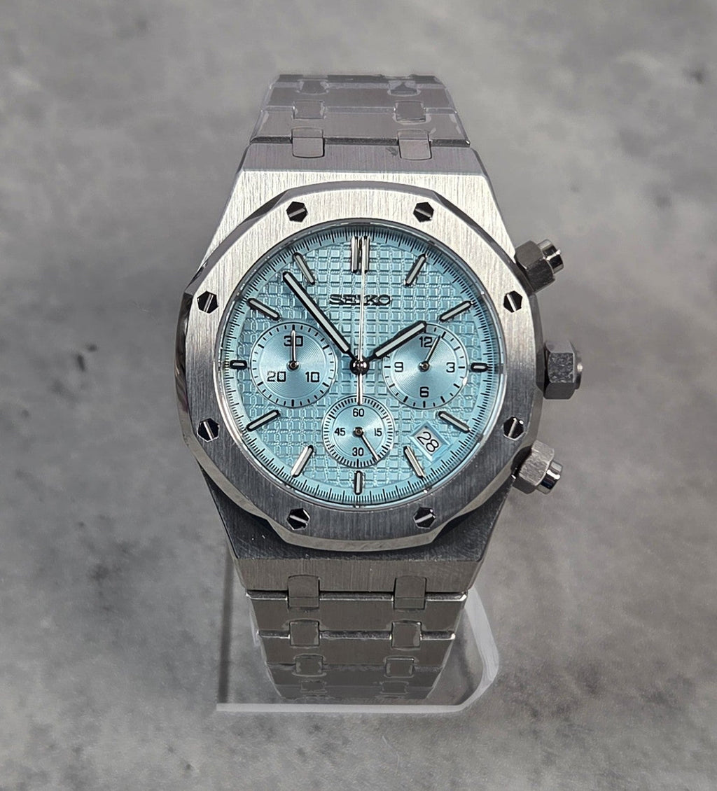 Luxury watch with a blue face and silver case on a gray background