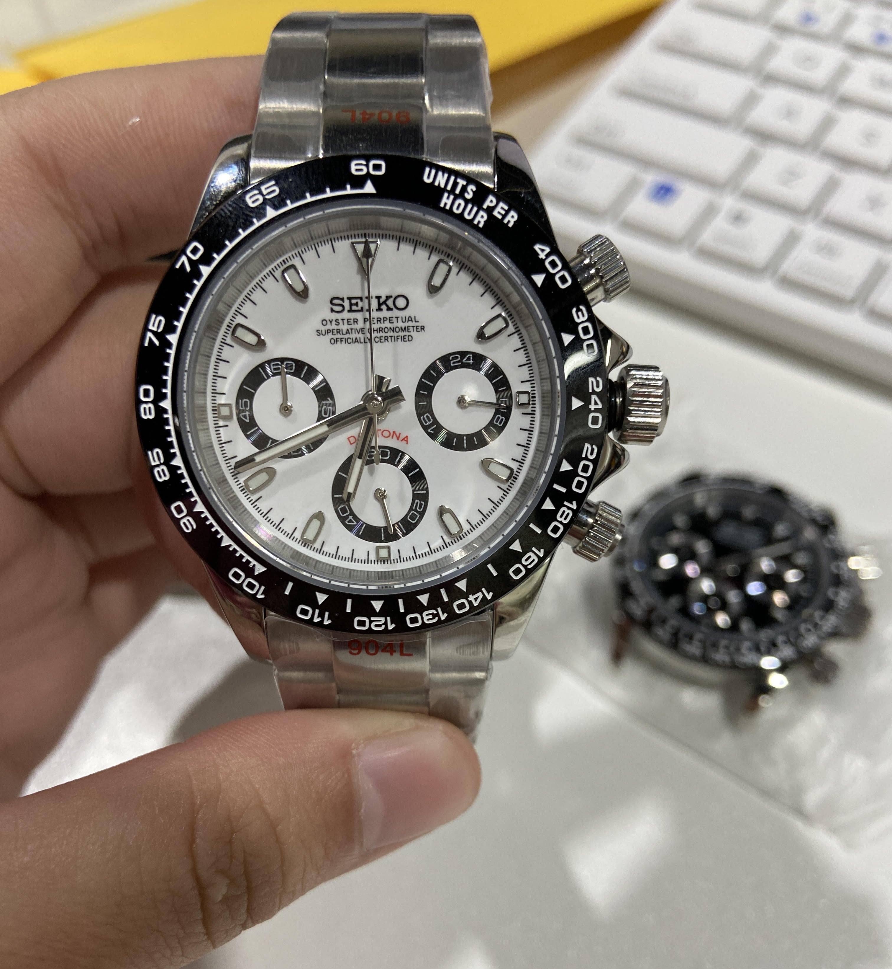Seiko watch held in a hand with a blurred keyboard in the background